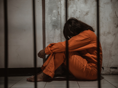 Woman hugging her knees in prison cell
